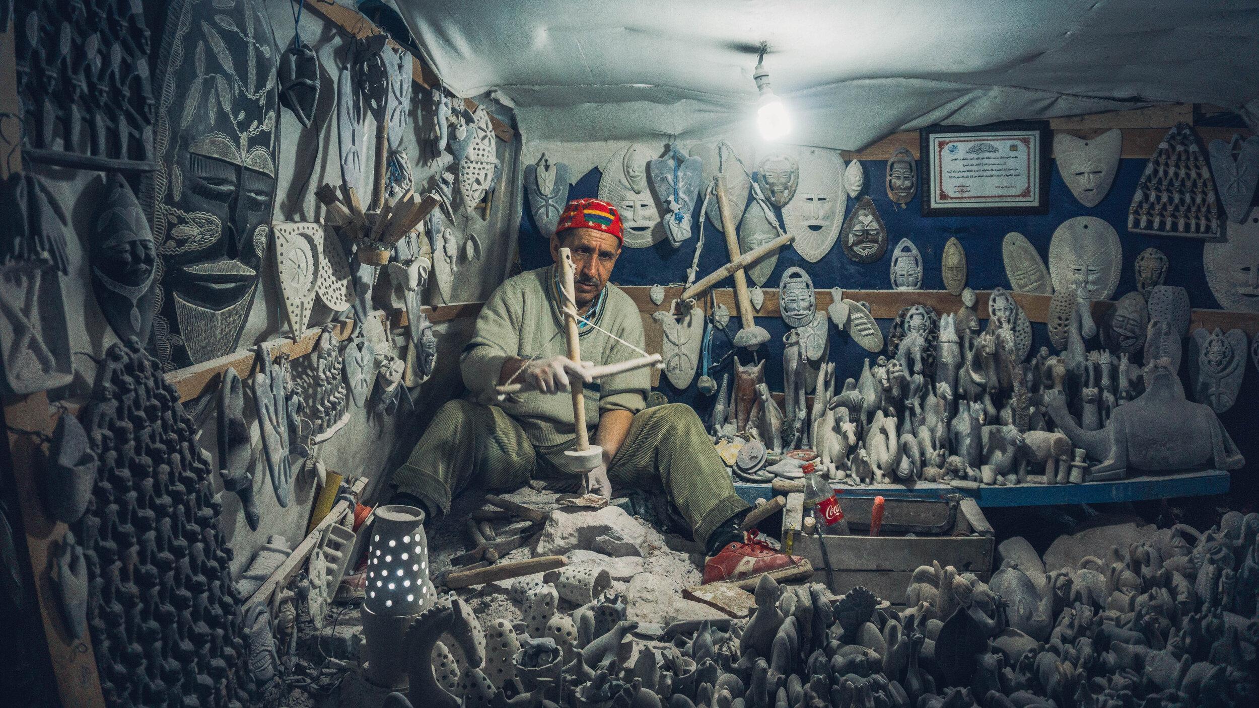 A Moroccan artisan hand-carving plaster masks and figures in his workshop